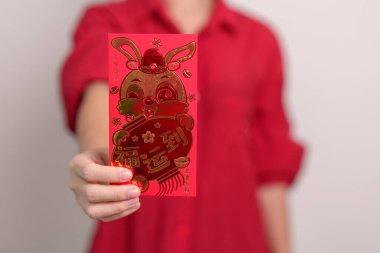 woman holding Chinese red envelope with golden rabbit and blessing word, money gift for happy Lunar New Year holiday. Chinese sentence means happiness, healthy, Lucky and Wealthy