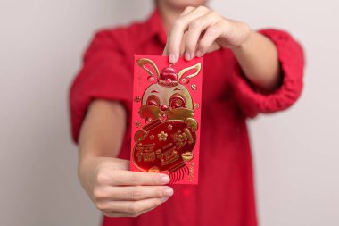 woman holding Chinese red envelope with golden rabbit and blessing word, money gift for happy Lunar New Year holiday. Chinese sentence means happiness, healthy, Lucky and Wealthy