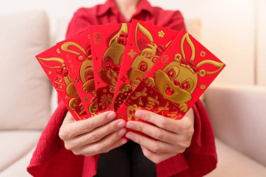 woman holding Chinese red envelope with golden rabbit and blessing word, money gift for happy Lunar New Year holiday. Chinese sentence means happiness, healthy, Lucky and Wealthy