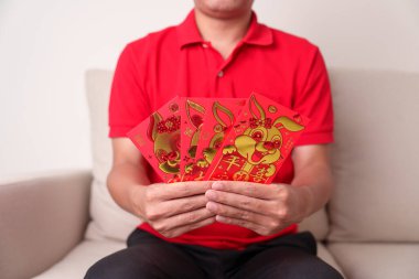 man holding Chinese red envelope with golden rabbit and blessing word, money gift for happy Lunar New Year holiday. Chinese sentence means happiness, healthy, Lucky and Wealthy