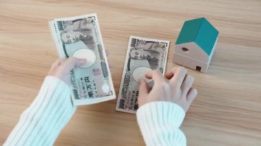 hand counting Japanese Yen banknote with House model. Real Estate, Home, Mortgage, Japan cash, Tax, Recession Economy, Inflation, Investment, finance and savings concepts