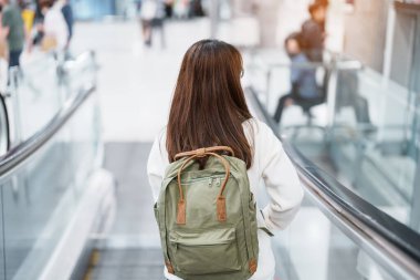 Asian woman traveler with backpack walking on escalator  in international airport. time to Travel, Vacation, trip and Transport concept