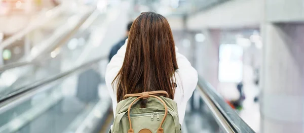 Asian woman traveler with backpack walking on escalator  in international airport. time to Travel, Vacation, trip and Transport concept