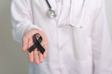 Melanoma ve cilt kanseri, aşı hasarı farkındalığı ayı ve huzur içinde yatma kavramları. Doktor elinde siyah kurdele tutuyor.