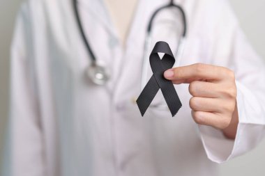 Melanoma ve cilt kanseri, aşı hasarı farkındalığı ayı ve huzur içinde yatma kavramları. Doktor elinde siyah kurdele tutuyor.