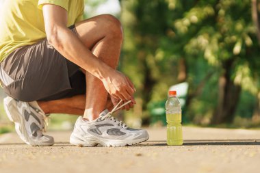 Koşu ayakkabılarını enerji içeceği suyuyla bağlayan genç bir atlet, erkek koşucu dışarıda koşmaya hazır, Asyalı sporcu parkta yürüyüş ve egzersiz yapıyor. Refah, refah ve spor kavramları
