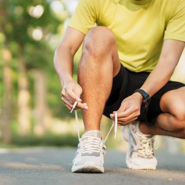 Parkta koşu ayakkabısı bağlayan genç bir atlet, erkek koşucu dışarıda yolda koşmaya hazır, Asyalı sporcu sabah yaya yolunda yürüyor ve egzersiz yapıyor. Refah ve spor kavramları