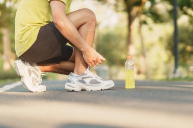 Koşu ayakkabılarını enerji içeceği suyuyla bağlayan genç bir atlet, erkek koşucu dışarıda koşmaya hazır, Asyalı sporcu parkta yürüyüş ve egzersiz yapıyor. Refah, refah ve spor kavramları