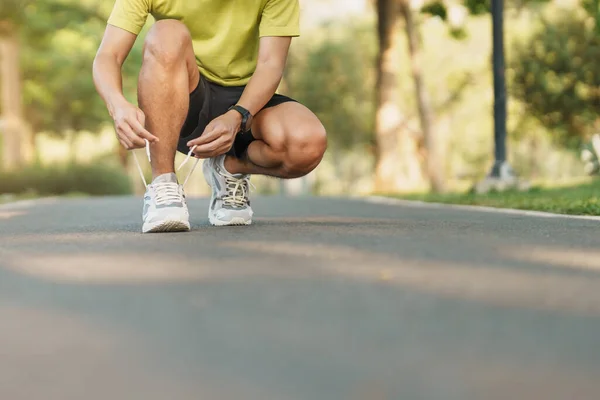 stock image Young athlete man tying running shoes in the park outdoor, male runner ready for jogging on the road outside, asian Fitness walking and exercise on footpath in morning. wellness and sport concepts