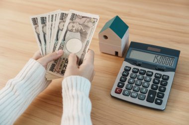Woman counting Japanese Yen banknote with House model. Real Estate, Home, Mortgage, Japan cash, Tax, Recession Economy, Inflation, Investment, finance and savings concepts