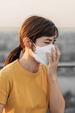 N95 solunum maskesi takan genç Asyalı kadın PM2.5 'u koruyor ve filtre ediyor veya şehirdeki kötü hava kirliliğine karşı partikül madde. Hava Kalite Endeksi, El Kaide, Sağlıksız, Sağlık Hizmetleri Konsepti