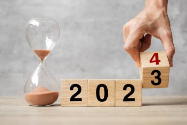 2023 'ten 2024' e kadar masa üzerinde kum saati yazılı el çevirme bloğu. Çözüm, zaman, plan, hedef, motivasyon, yeniden başlatma, geri sayım ve yeni yıl tatili kavramları