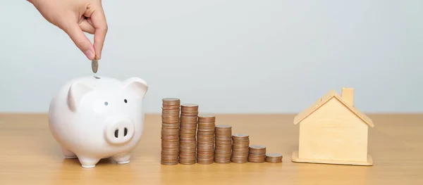 Money Saving, Property investment, House Mortgage and Real Estate Financial concepts. hand putting coin into piggy bank with Home model, Money stack Counting arrangement for deposit and Tax