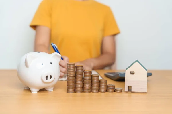 Money Saving, Property investment, House Mortgage and Real Estate Financial concepts. woman with coins stack piggy bank and Home model, Money stack Counting arrangement for deposit and Tax