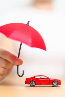 İş kadını eli kırmızı şemsiye tutuyor ve masada kırmızı araba oyuncağını örtüyor. Araba sigortası, garanti, onarım, finans, bankacılık ve para kavramı