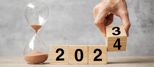 2023 'ten 2024' e kadar masa üzerinde kum saati yazılı el çevirme bloğu. Çözüm, zaman, plan, hedef, motivasyon, yeniden başlatma, geri sayım ve yeni yıl tatili kavramları