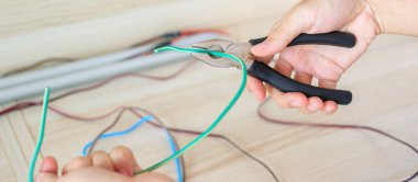 Elektrikçi penseyle elektrik kablolarını kesiyor, prizlerin elektrik kablolarını yerleştiriyor. Tamir, yenileme, onarım, hizmet ve konut kavramlarının geliştirilmesi