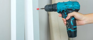 Evde mobilya montajı yapan kablosuz tornavida kullanan bir adam, işte elektrikli tornavida kullanan bir marangoz.