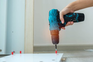 Evde mobilya montajı yapan kablosuz tornavida kullanan bir adam, işte elektrikli tornavida kullanan bir marangoz.