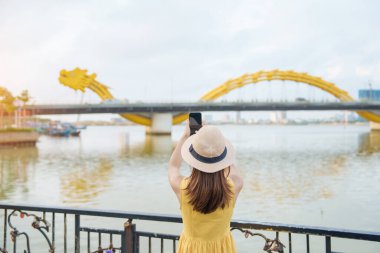 Da Nang 'a gelen sarı elbiseli kadın gezgin. Turistler nehir manzarasını geziyor. Aşk köprüsünde Ejderha köprüsü var. Şehir simgesi ve popüler. Vietnam ve Güneydoğu Asya seyahat kavramı