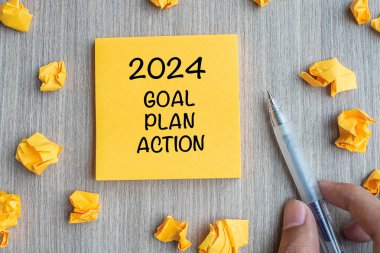 2024 Gol, Plan, Eylem kelimesi sarı notta İşadamı 'nın elinde kalem ve kağıt parçalarını ahşap masa arkasında tutarken. Yeni Yıl Yeni Başlangıç, Çözümler, Strateji Konsepti
