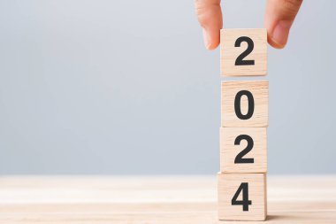 Masa arkasında 2024 yazılı ahşap küp bloğu olan el ele tutuşmalar. Çözüm, plan, gözden geçirme, hedef, başlangıç ve yeni yıl tatili kavramları