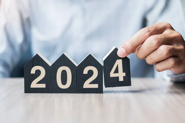 stock image Businessman hands holding 2024 Happy New Year with house model on table office. New House, Financial, Property insurance, real estate, savings and New Year Resolution concepts