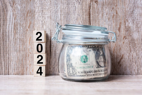 2024 Happy New Year with US dollar money glass American on wood table background. business, investment, retirement planning, finance, Saving and New Year Resolution concepts