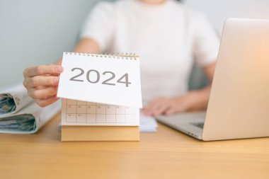 2024 Yıllık Takvim dizüstü bilgisayar kullanan bir iş kadınıyla masada. Geri sayım, Mutlu Yıllar, Çözünürlük, Hedefler, Plan, Eylem, Görev ve Mali Konsept