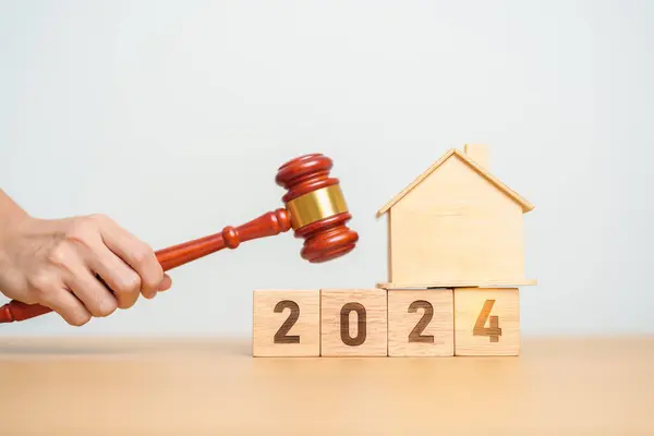 Real Estate Law, Home Insurance, property Tax, Auction and Bidding concepts. 2024 year block with small toy house model with gavel justice hammer on desk in courthouse.