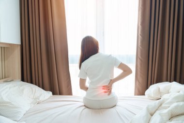 Evde yatakta otururken sırtı ağrıyan bir kadın. Piriforis Sendromu, Düşük Sırt Ağrısı ve Omurga Baskısı nedeniyle uyandıktan sonra kas ağrısı çeken yetişkin bir kadın. Sağlık Medikal Konsepti