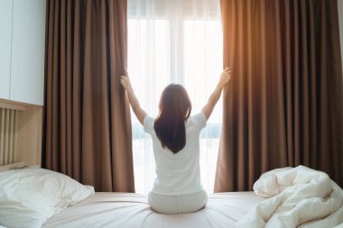 Mutlu kadın uyandıktan sonra yatağa uzanıyor, genç yetişkin kadın kollarını kaldırıyor ve sabahın erken saatlerinde pencereye bakıyor. Rahatlayın ve güzel bir gün geçirin.