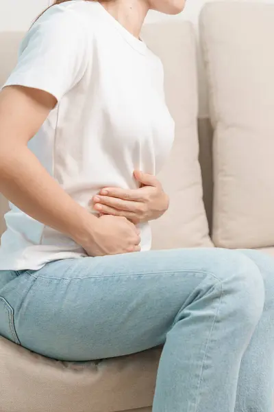 Woman having abdomen pain on the sofa at home. Liver cancer and Tumor, kidney cancer, Jaundice, Viral Hepatitis, Cirrhosis, Failure, Enlarged, Hepatic Encephalopathy, Stomach and health concept