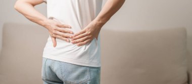 Evdeki koltukta otururken sırt ağrısı çeken bir kadın. Piriforis Sendromu, bel ağrısı ve omurga baskısı nedeniyle kas ağrısı olan yetişkin bir kadın. Ofis sendromu ve tıbbi konsept