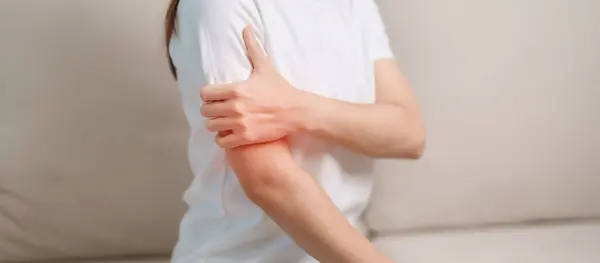 Woman having arm pain during sitting on couch at home, muscle injury and ache. Health and medical concept