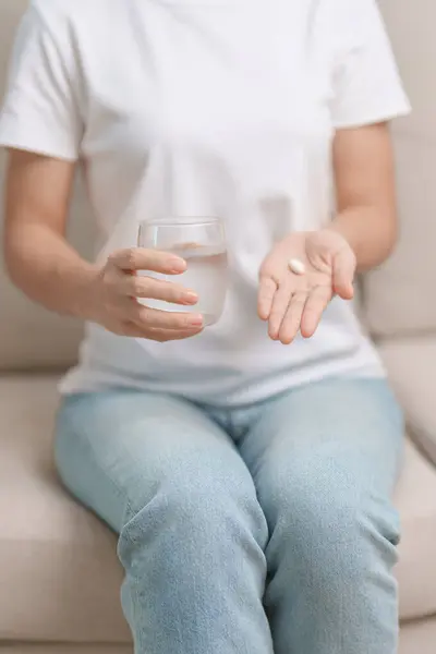 woman hand holding medicine painkiller pill and water glass on the sofa at home, taking for headaches,  stomach ache, Diarrhea Pain from food poisoning, Endometriosis, Hysterectomy and Menstrual