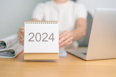 2024 Yıllık Takvim dizüstü bilgisayar kullanan bir iş kadınıyla masada. Geri sayım, Mutlu Yıllar, Çözünürlük, Hedefler, Plan, Eylem, Görev ve Mali Konsept