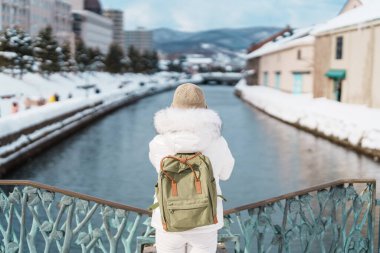 Otaru 'yu ziyaret eden kadın turist, süveter giyen mutlu gezgin kış mevsiminde Otaru kanalını geziyor. Japonya 'nın Hokkaido şehrinde önemli ve popüler bir yer. Seyahat ve Tatil kavramı