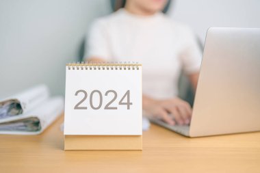 2024 Yıllık Takvim dizüstü bilgisayar kullanan bir iş kadınıyla masada. Geri sayım, Mutlu Yıllar, Çözünürlük, Hedefler, Plan, Eylem, Görev ve Mali Konsept