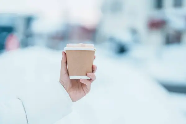 woman tourist holding hot Coffee or Tea paper cup with snow in winter season during travel in Niseko. landmark and popular for attractions in Hokkaido, Japan. Travel and Vacation concepts