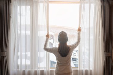 Kazaklı genç bir kadın kış mevsiminde pencereden dışarı bakıyor mutlu kadın kollarını kaldırıyor ve sabah evde ya da dairede uyandıktan sonra esniyor. Yaşam tarzı ve rahatlatıcı kavramlar