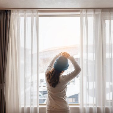 Kazaklı genç bir kadın kış mevsiminde pencereden dışarı bakıyor mutlu kadın kollarını kaldırıyor ve sabah evde ya da dairede uyandıktan sonra esniyor. Yaşam tarzı ve rahatlatıcı kavramlar