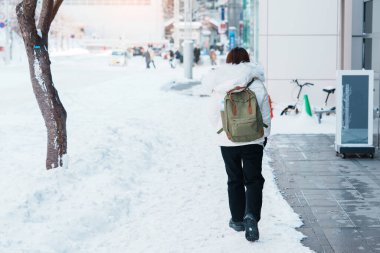 Buzlu havada karla kaplı yolda yürüyen mutlu gezgin, Sapporo şehrinde kadın turist gezisi, Hokkaido, Japonya Kış Seyahati ve Tatil Konsepti