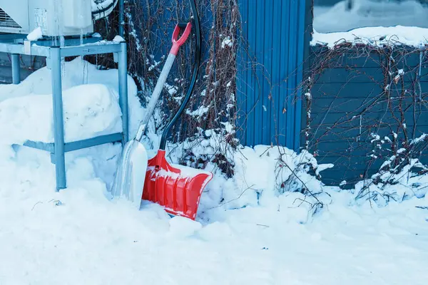 Red shovel for removes snow from the road and clears the sidewalk in winter season. Cleaning and clearing roads after snowfalls and blizzards