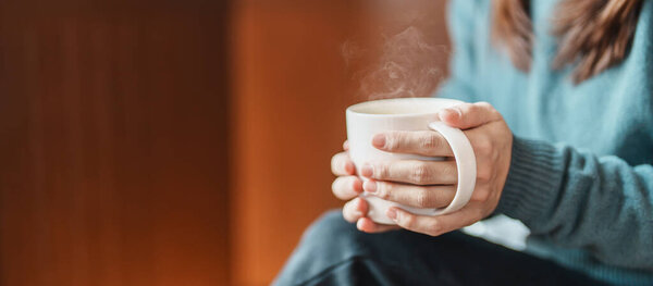 Молодая женщина пьет горячий чай зимой, женщина держит руку и наслаждается чашкой кофе дома утром