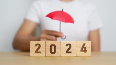 El ele tutuşup kırmızı şemsiye tutmak ve 2024 yıllık bloğu kaplamak. Sigorta, koruma, güvenlik ve yeni yıl tatili kavramları