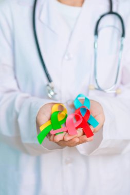 Dünya Kanser Günü, 4 Şubat. Doktor, mavi, sarı, kırmızı, yeşil, beyaz, pembe ve gri renkli kurdeleleri yaşayan ve hastalıkları desteklemek için tutuyor. Sağlık, Sağlık, Farkındalık ve Sigorta kavramı