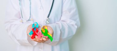 Dünya Kanser Günü, 4 Şubat. Doktor, mavi, sarı, kırmızı, yeşil, beyaz, pembe ve gri renkli kurdeleleri yaşayan ve hastalıkları desteklemek için tutuyor. Sağlık, Sağlık, Farkındalık ve Sigorta kavramı