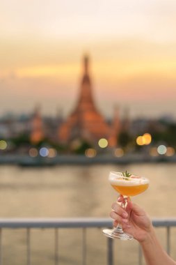 Turist gün batımında Wat Arun Tapınağı 'na giderken kokteyl kadehini gösteriyor. Gezgin çatı katındaki bardan Temple of Dawn' ı ziyaret ediyor. Seyahat güzergahı Bangkok, Tayland ve Güneydoğu Asya