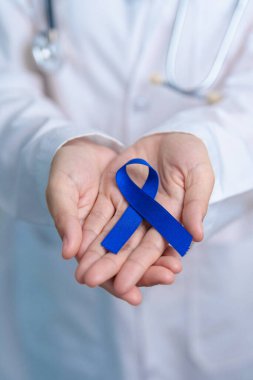 March Colectal Kanser Farkındalığı Ayı. Koyu mavi kurdeleli bir doktor. Yaşayan ve hastalıklı insanları destekliyor. Sağlık, umut ve Dünya Kanser Günü konsepti